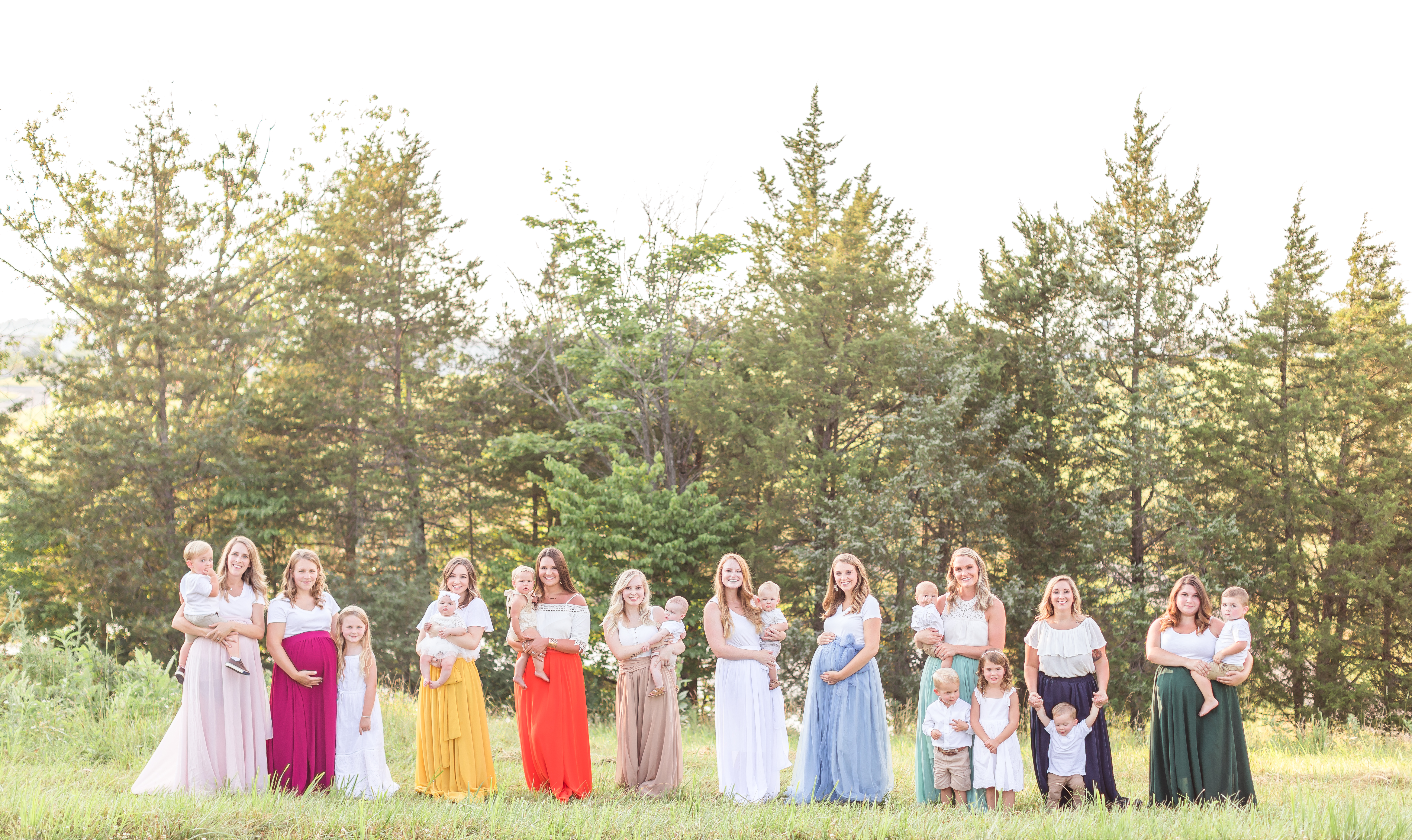 Mothers of all ages stand together holding their children, maternity bellies, and friends in long, flowy skirts of all colors as part of Amanda Shrader's the Skirt Project photoshoot.